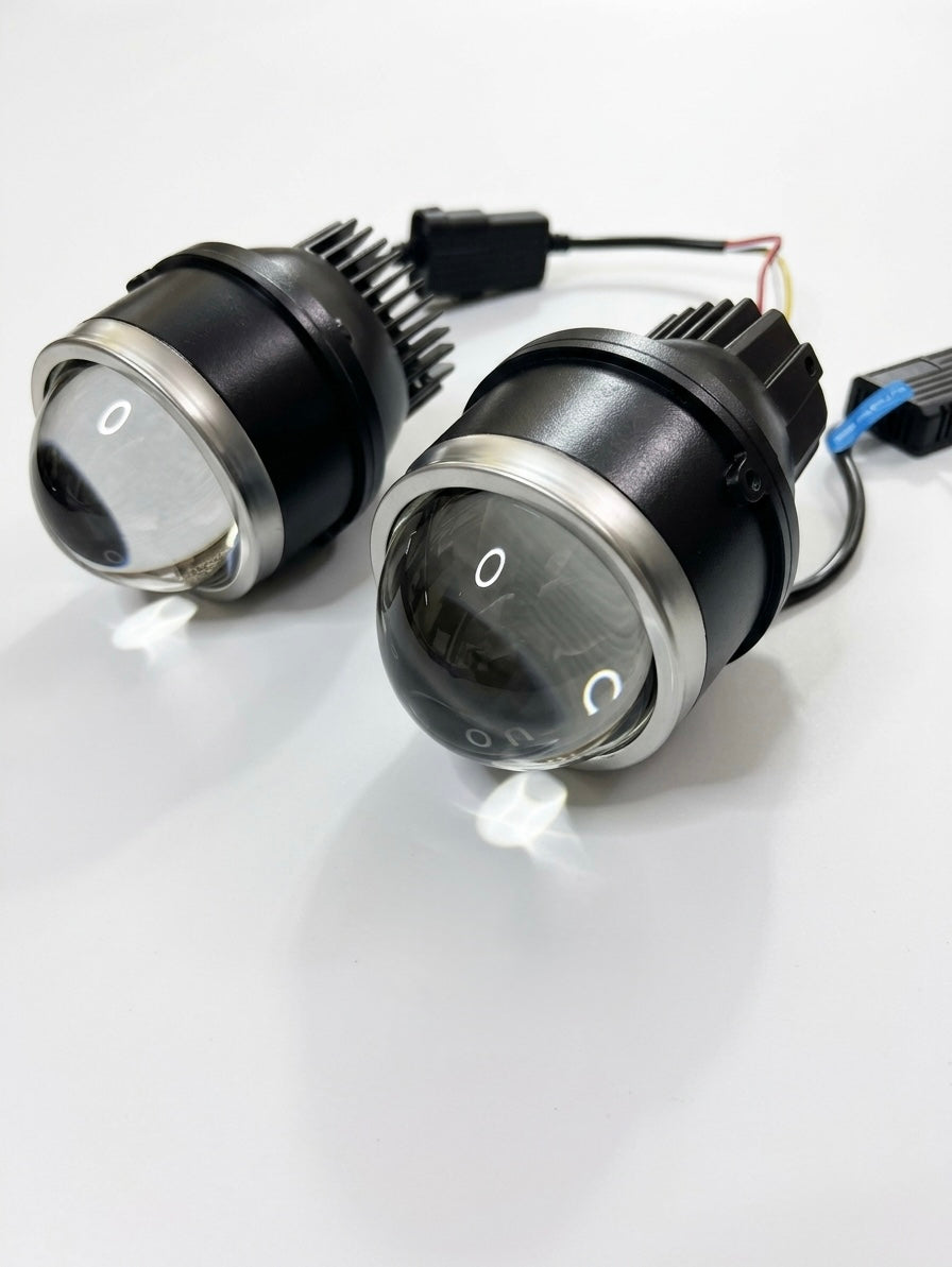 Two black automotive LED headlight pods with clear lenses and silver trim, shown on a white reflective surface with their wiring harnesses visible.